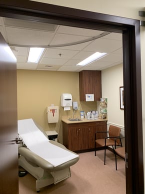 Photo of a hospital exam room with a single reclining exam seat and two LED lighting fixtures above, showing a healthcare energy efficiency initiative.