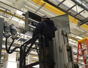 Working on retrocommissioning a facility using energy efficiency tactics, shows a man on a platform working in an industrial looking facility